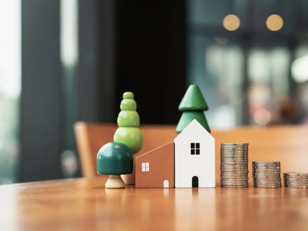 Model house and tree beside stacked coins